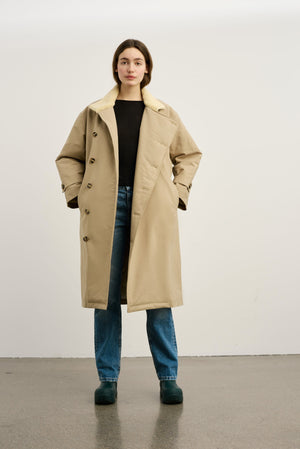 A model wearing a beige oversized coat with a shearling collar, paired with a black top and blue jeans, showcasing MEOTINE style.