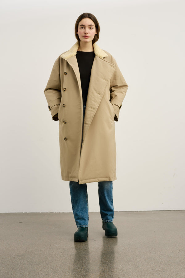 A model wearing a beige MEOTINE coat with a soft collar, paired with a black top and blue jeans, standing against a neutral background.