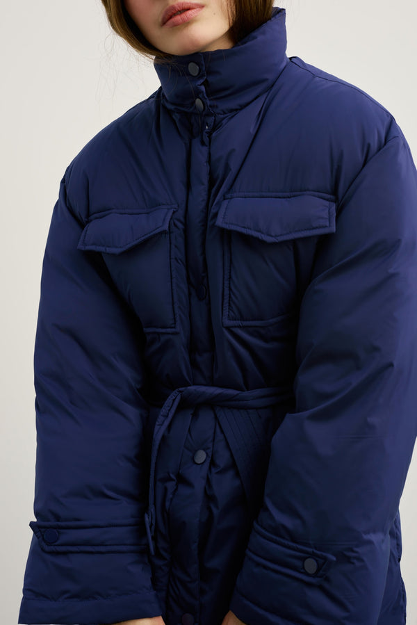 A model wears a navy blue oversized puffer jacket with a belted waist and large pockets, showcasing MEOTINE's stylish design.