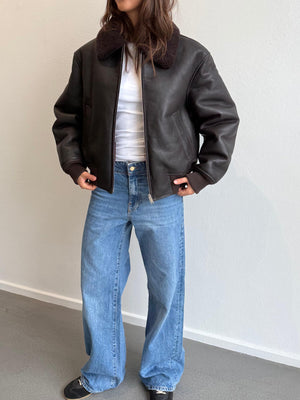 A model wears a stylish brown leather bomber jacket with a cozy collar, paired with wide-leg jeans, showcasing MEOTINE's chic design.