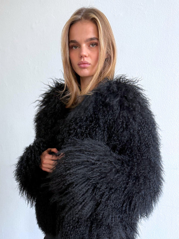 A model showcases a stylish black fluffy coat by MEOTINE, featuring long, textured sleeves and a cozy, oversized fit.