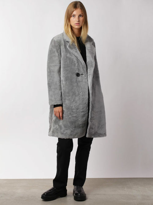 A model wears a stylish gray faux fur coat by MEOTINE, paired with black pants and shoes, set against a neutral background.