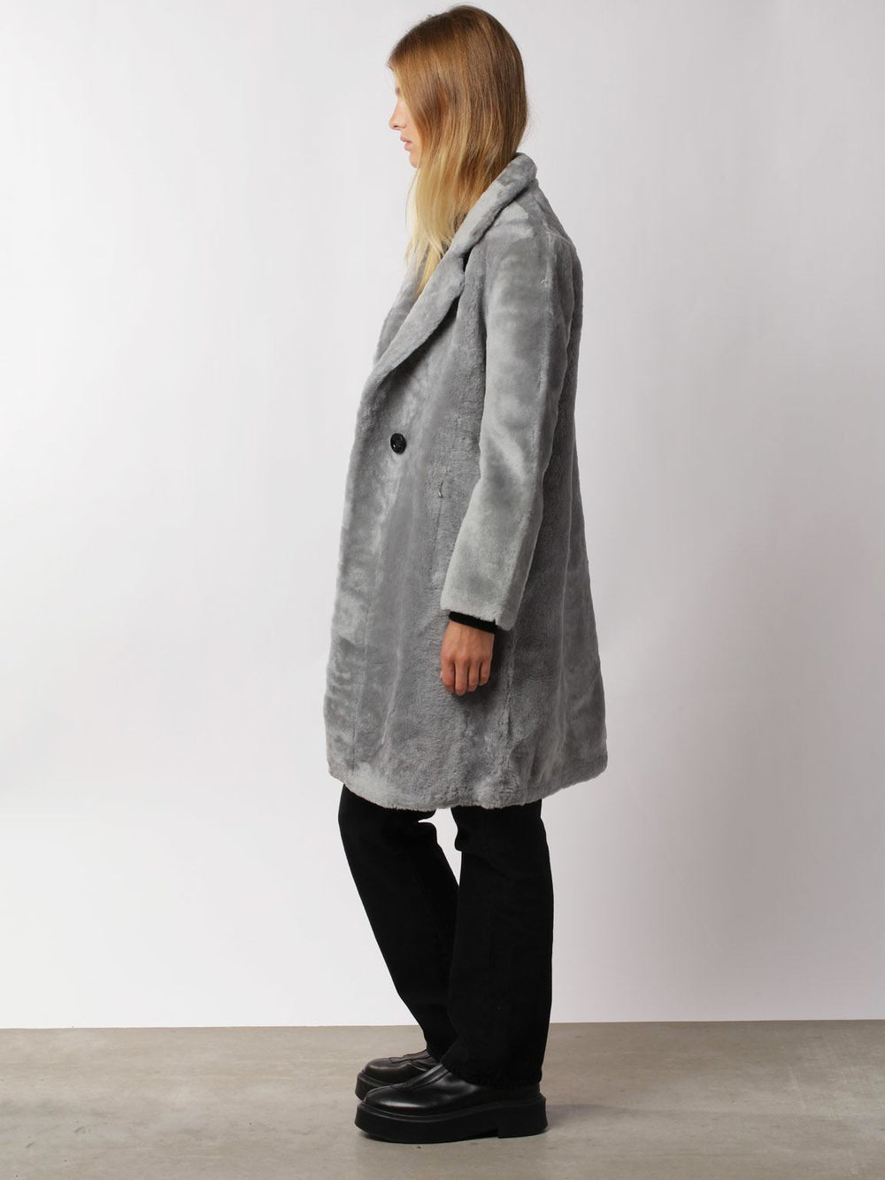 A model wears a stylish gray faux fur coat by MEOTINE, paired with black pants and shoes, set against a neutral background.