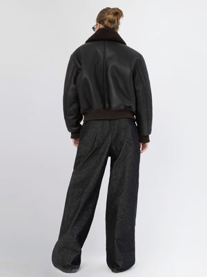 A model wearing a black leather bomber jacket with a brown collar and loose-fitting dark denim pants, showcasing MEOTINE's style.