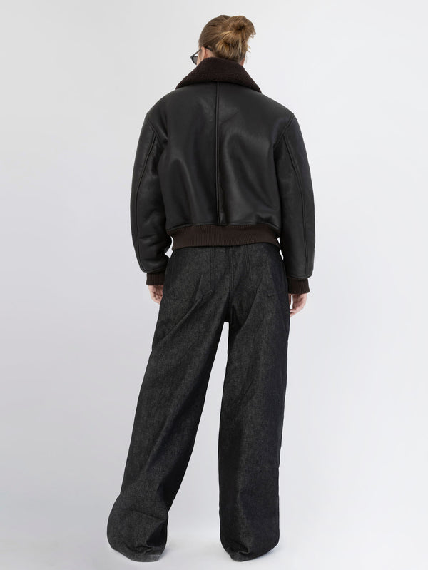 A model wearing a black leather bomber jacket with a brown collar and loose-fitting dark denim pants, showcasing MEOTINE's style.