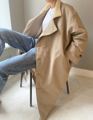 A person sits casually in a chair, wearing a beige MEOTINE coat with a soft collar, paired with light blue jeans.