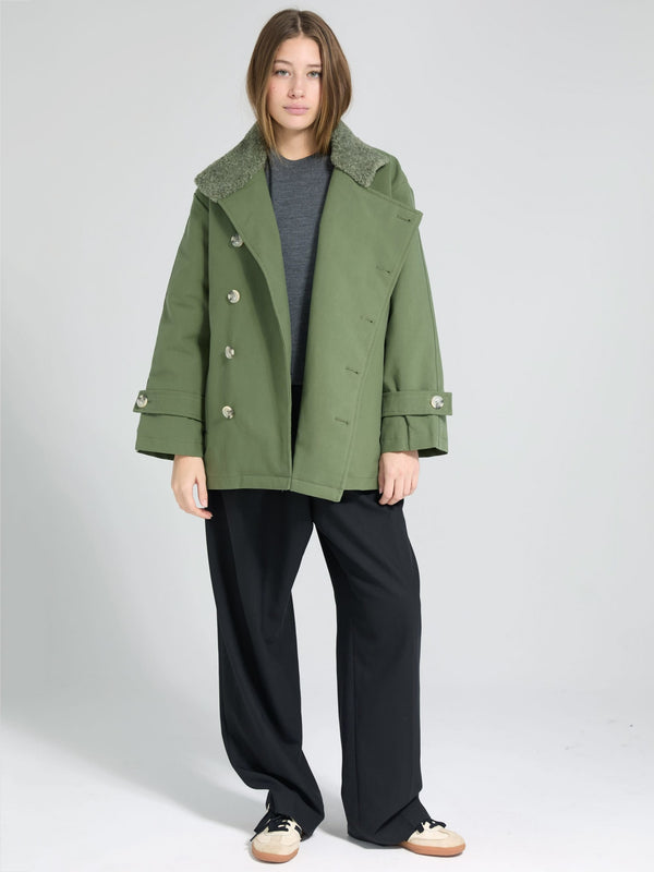 A model wears a stylish green coat with a fur collar, paired with a gray top and black wide-leg pants, showcasing MEOTINE's chic design.