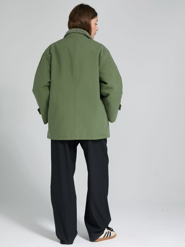 A model wearing a green oversized jacket with a cozy collar, paired with black wide-leg pants, showcasing MEOTINE's stylish design.