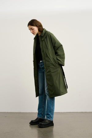 A model wearing a long olive green coat over a black top and blue jeans, showcasing MEOTINE's stylish outerwear.