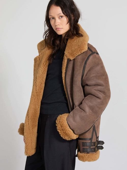 A model wears a stylish brown shearling jacket with a cozy tan collar and cuffs, showcasing MEOTINE's chic design.