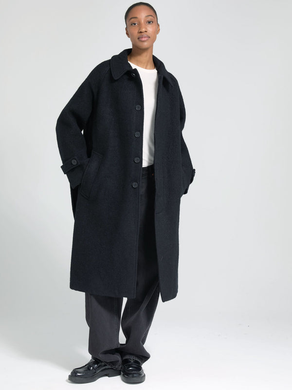 A model showcases a stylish black oversized coat by MEOTINE, paired with a simple white top and loose black trousers.