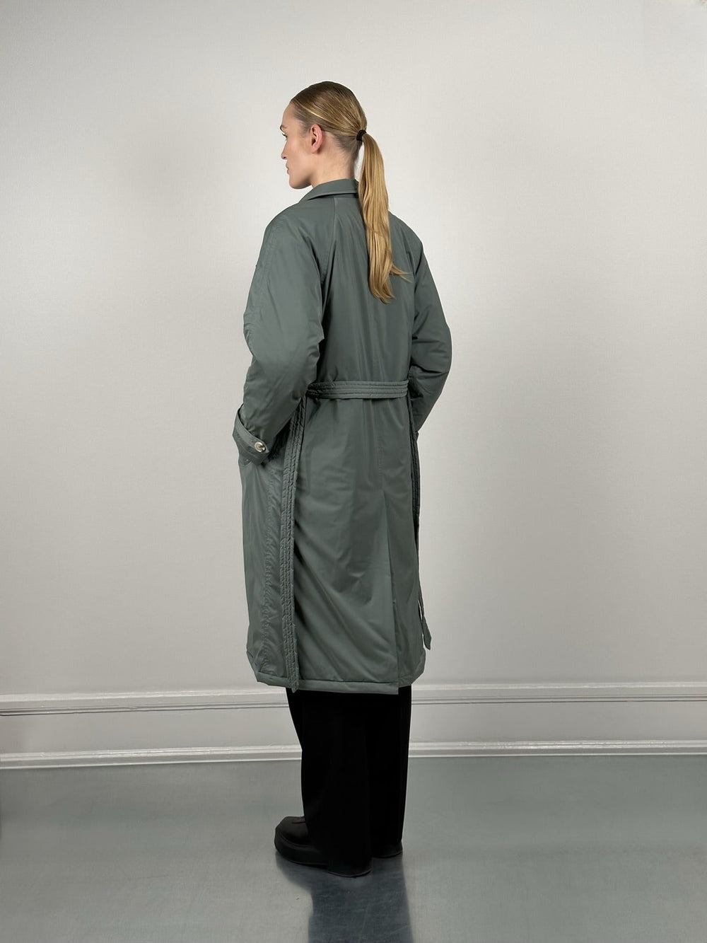 A model stands confidently in a stylish, oversized green trench coat by MEOTINE, paired with black pants and shoes.