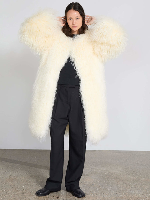 A model wears a fluffy, oversized cream coat paired with black trousers, showcasing MEOTINE's cozy and stylish outerwear.