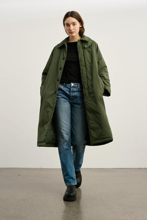 A model walks confidently in a long olive green coat paired with a black top and blue jeans, showcasing MEOTINE's stylish outerwear.