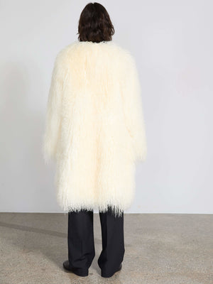 Fluffy white coat with a long silhouette, featuring a soft texture, styled with black pants. A chic piece by MEOTINE.