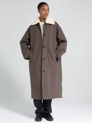 A model stands in a long brown coat with a white fur collar, showcasing MEOTINE's stylish and cozy outerwear design.