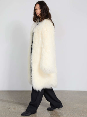 A model showcases a cozy, oversized white faux fur coat by MEOTINE, paired with black pants, set against a minimalist background.