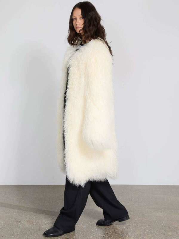 A model showcases a cozy, oversized white faux fur coat by MEOTINE, paired with black pants, set against a minimalist background.