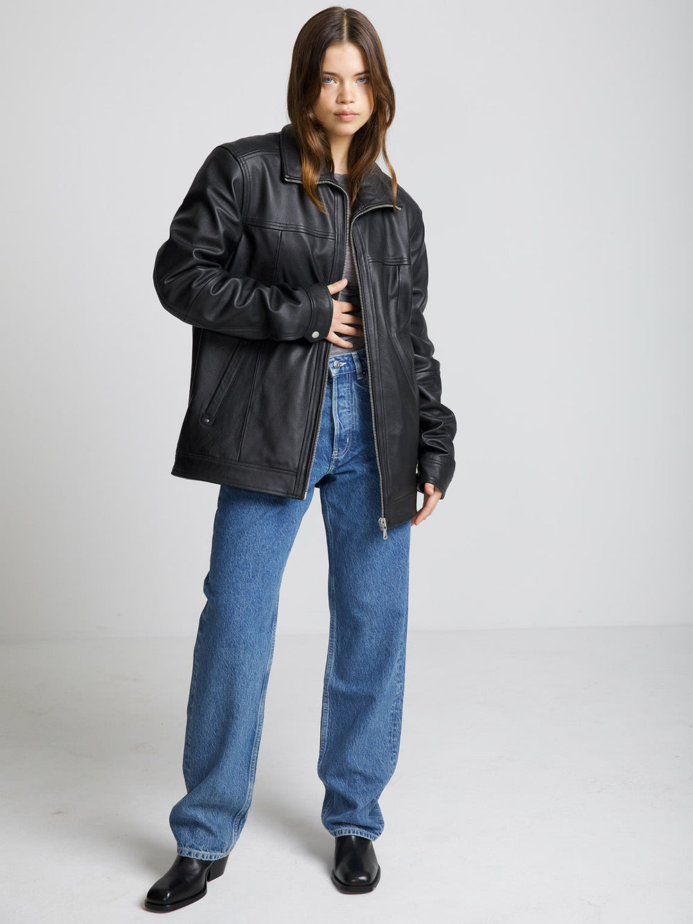 A model wearing a black leather jacket from MEOTINE, paired with blue jeans and black boots, posing against a neutral background.